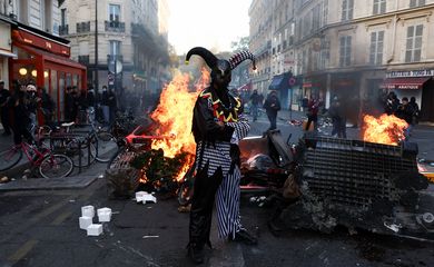 A demonstrator wearing a costume stands in front of burning flames, in Paris, France, October 18, 2026. REUTERS/Abdul Saboor