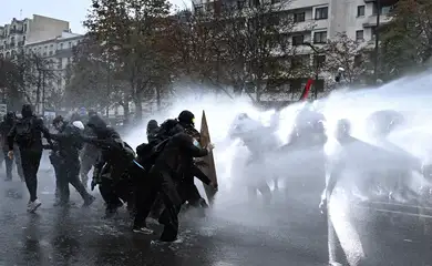 Protesters take cover behind a plywood board as French riot police use a water canon amid clashes during an authorised demonstration organised by labour unions in Paris as part of nationwide protests called by the